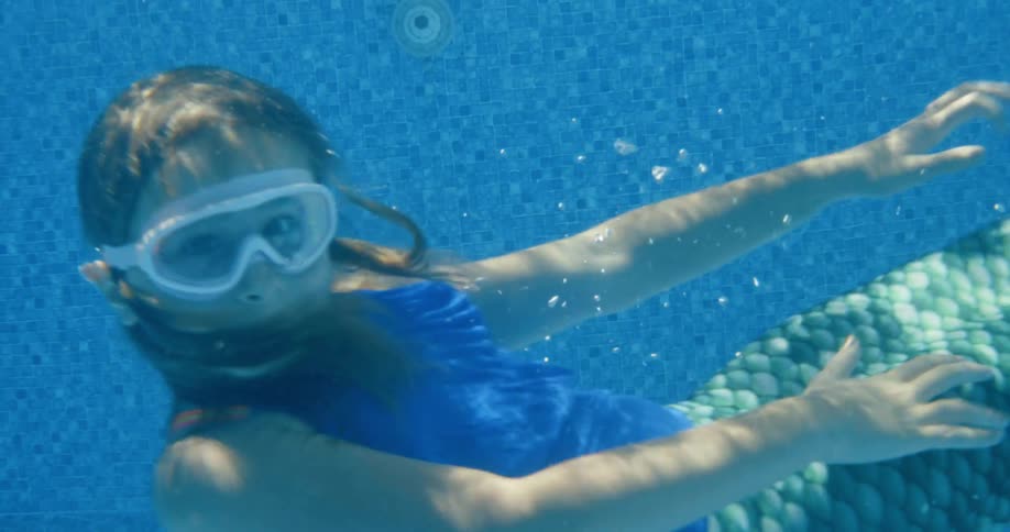 A young girl wears a swimsuit that looks like mermaid fins as she swims in her pool