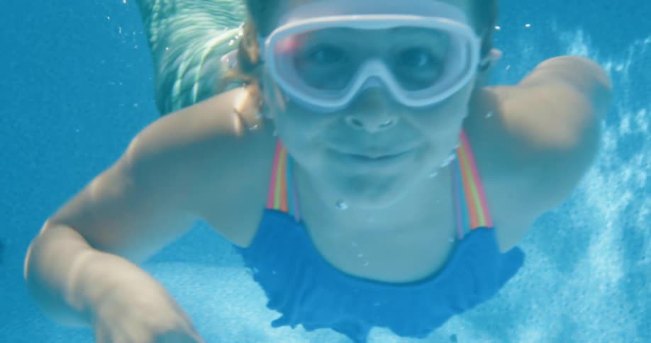 A girl is swimming underwater in the pool wearing a mermaid costume