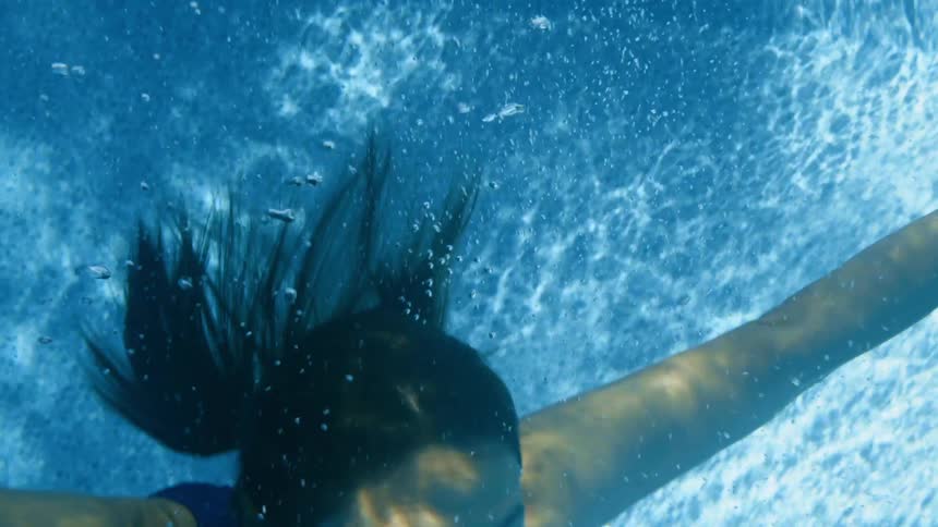 A woman in a swimming dives underwater while facing the camera