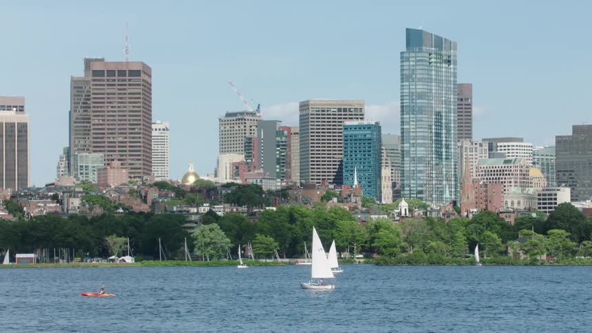 Sailboats sailing on the river in front of high rise buildings in the city