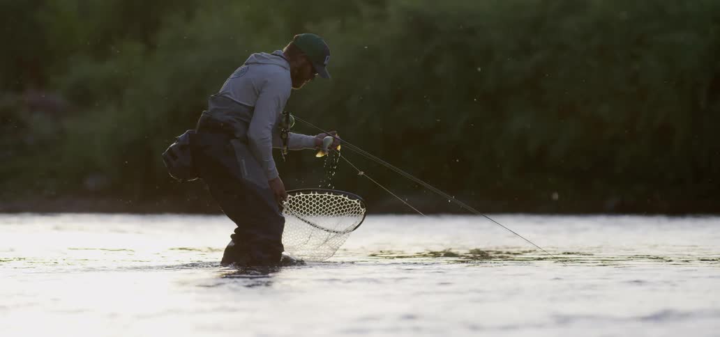 A man fishing in the water picks a fish up out of his net