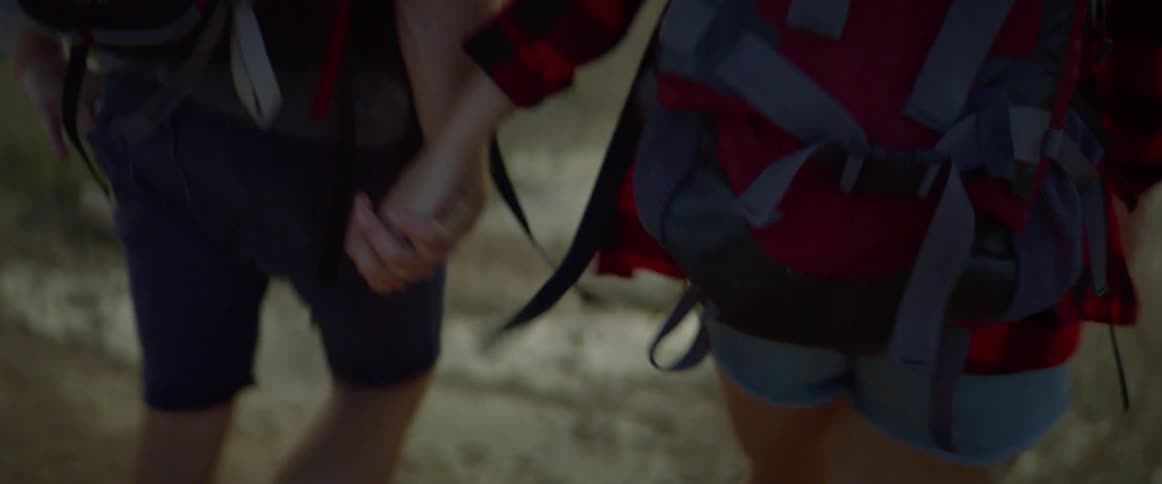 A man and woman hold hands as they hike through a forest