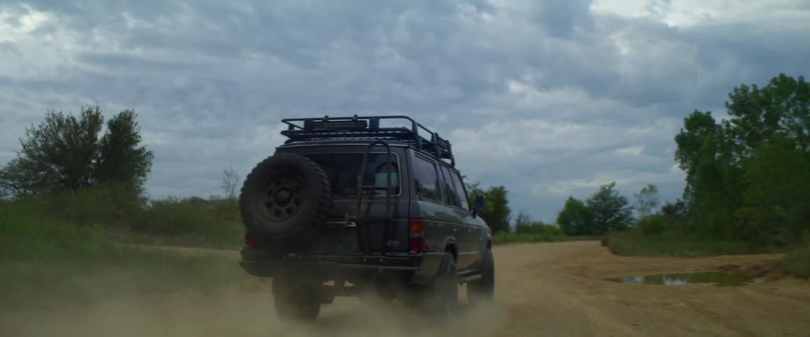 An suv style vehicle drives along a rural dirt road