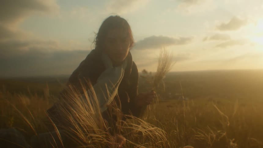A woman is looking at plants in a grassland area