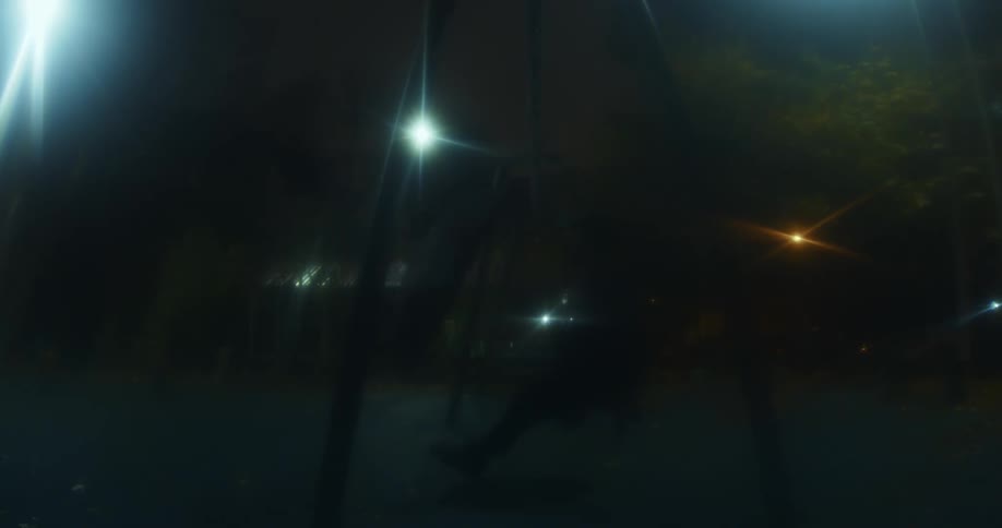 A person is swinging on a swing in the dark with lights in the background