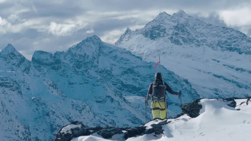 A mountaineer looks out at a mountain valley while standing atop a mountain cliff