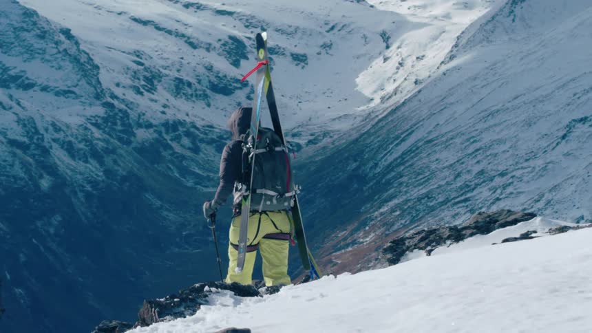 A mountaineer descends a snowy mountain slow during the day