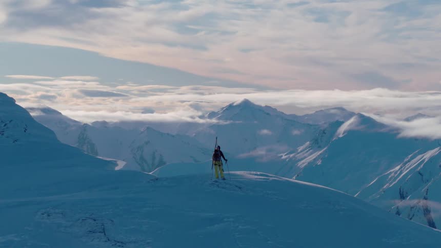 Skier holds skis and poles while standing on top of a snowy mountain