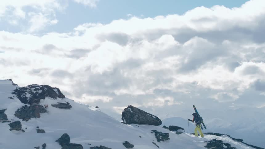 A mountaineer hikes up a rocky snow covered mountain slope on a bright day