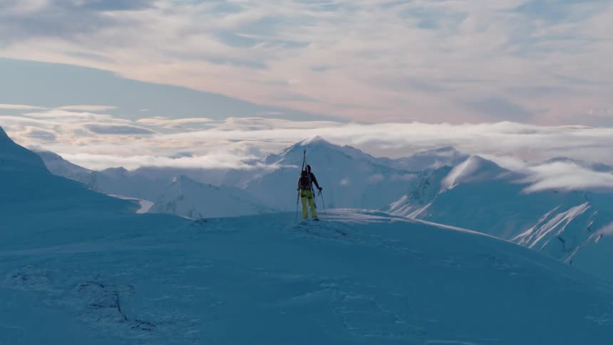 Person stands on high peak above snow covered mountain range