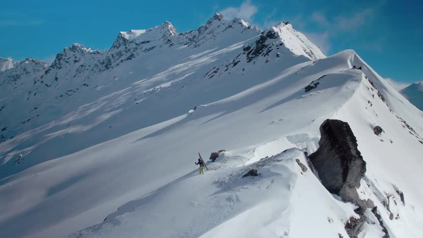 A skier walks near the peak of a huge snow covered mountain with his ski gear