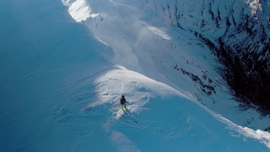 Skier stands on snow covered cliff over valley