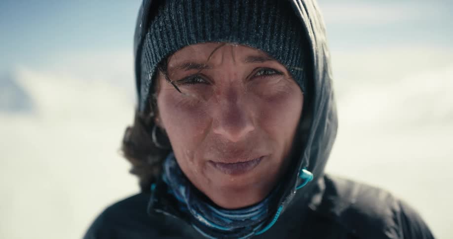 A woman standing in heavy wind in the arctic stares into the camera