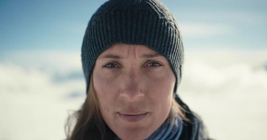 A woman stands outside as snow blows across her face