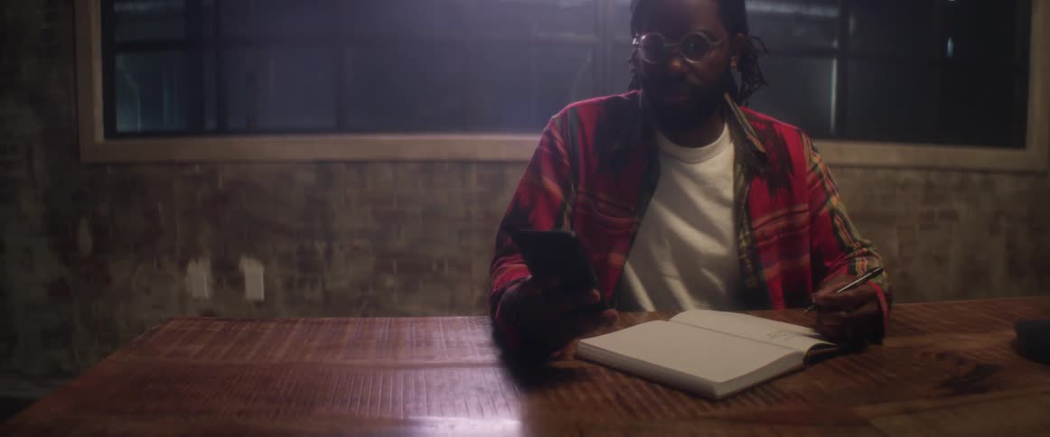 A young man is writing in a book and then picks up his cell phone when he gets a notification