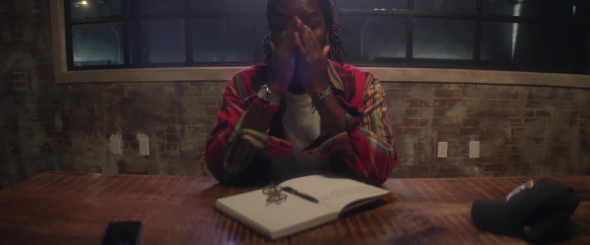 A man sits at a table with a book and pen and drops his head in frustration