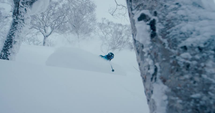 Person skis down hill between trees