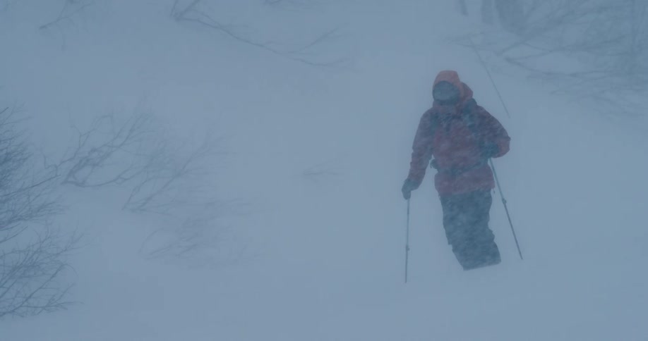 A hiker walking over snow in the wilderness during a blizzard