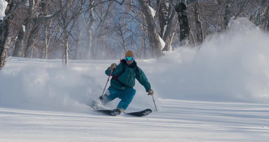 A skier in a blue coat speeding down a snowy mountainside on a winter day