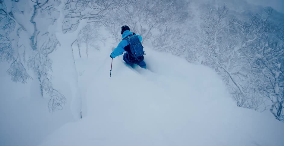 A person with a helmet and a backpack skiing down a snowy slope