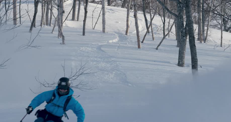 Skier slides down the snow covered hill through the trees