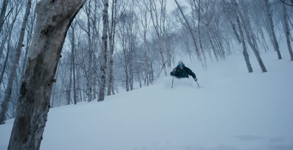 Skier slides down a snow covered hill in the mountains through the forest