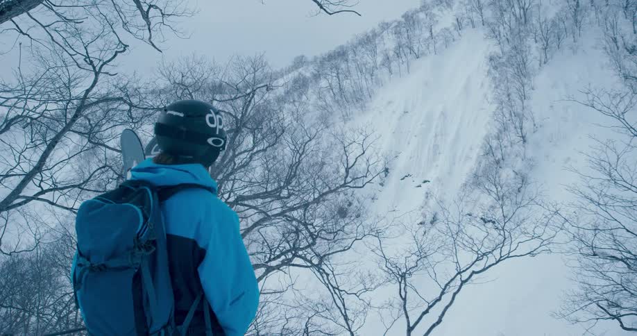 Skier stands looking toward snow covered mountain slope