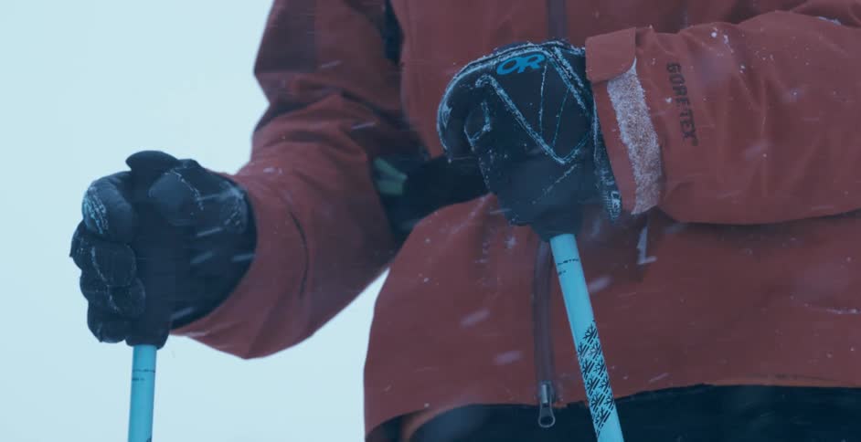A skier stands still and hold ski poles as snow falls down heavily