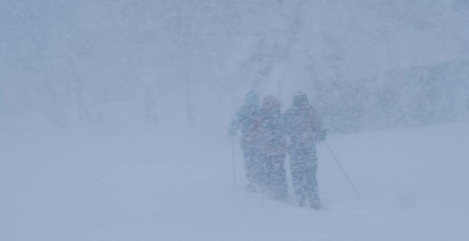 Skiers stay close together as they try to walk on a mountain during a snow storm