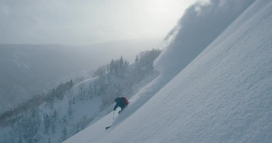 A person skis down a steep snow covered mountain side
