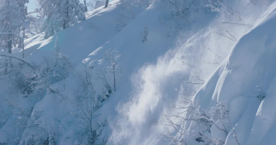 Skier jumps down steep snow covered mountain slope causing small avalanche