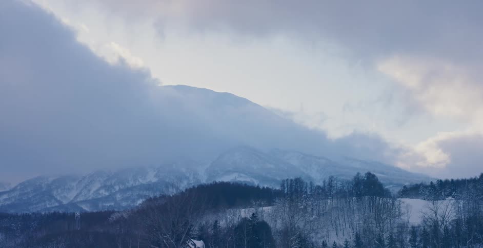 Light fog sets over a snow covered forest and mountain range