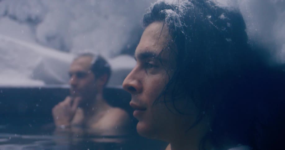 Two men sitting in a water spring with snow falling