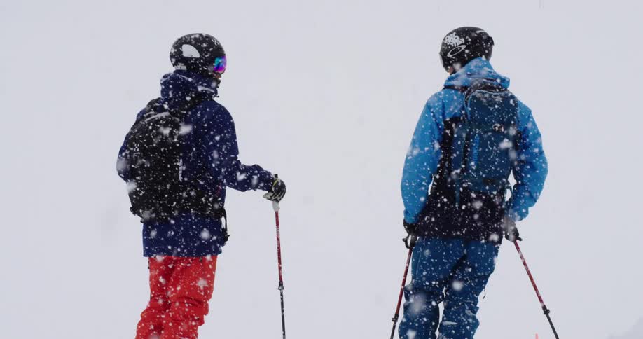 Two people are standing outdoors with ski equipment