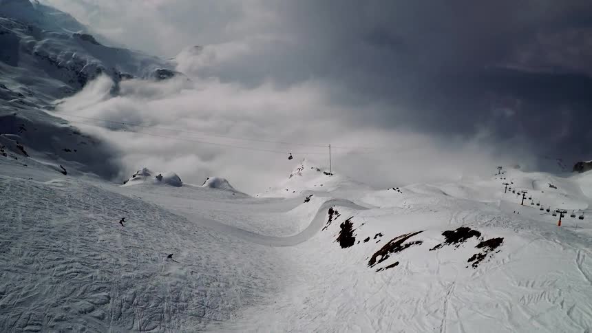 Skiers ski down slope near low lying clouds toward ski lift