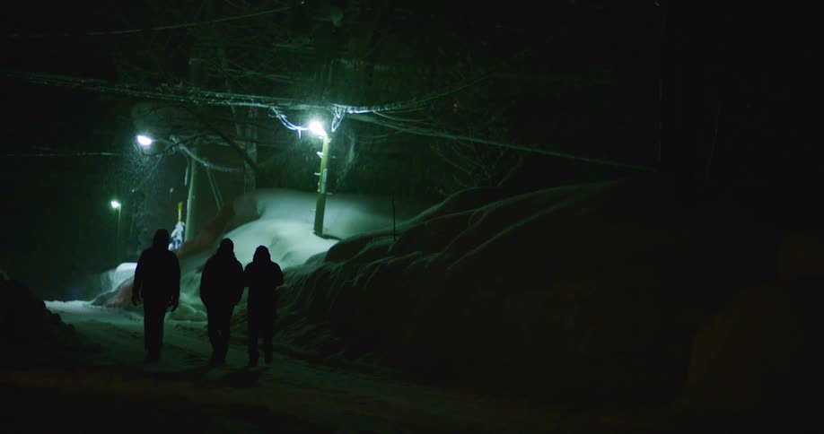 Three people walking outside at night as snow falls