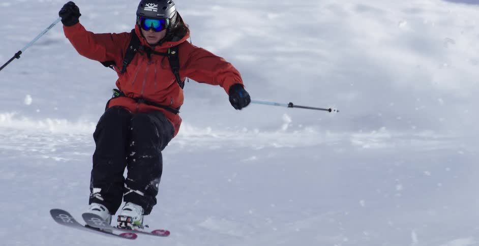 A skier crouches down as he comes around a curve and stands back up to jump
