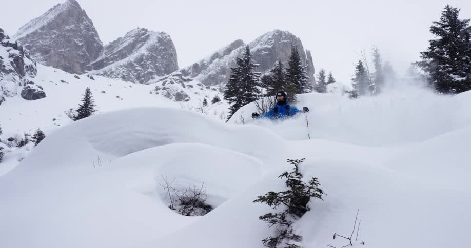 A skier in a blue coat going over a jump and crashing in snowy mountains