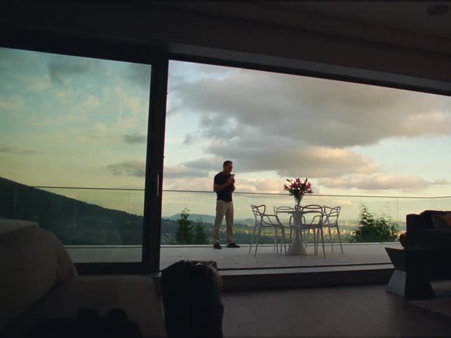 Man practicing golf stance while talking on a smartphone in the balcony at home