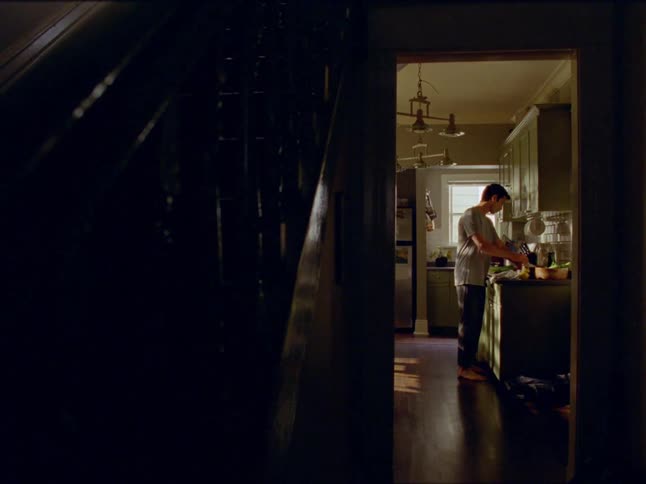 A man stands while cutting food on a counter in his kitchen
