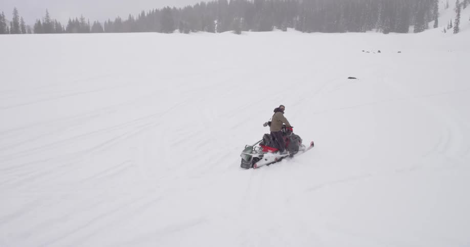 A man rides a snowmobile down a hill