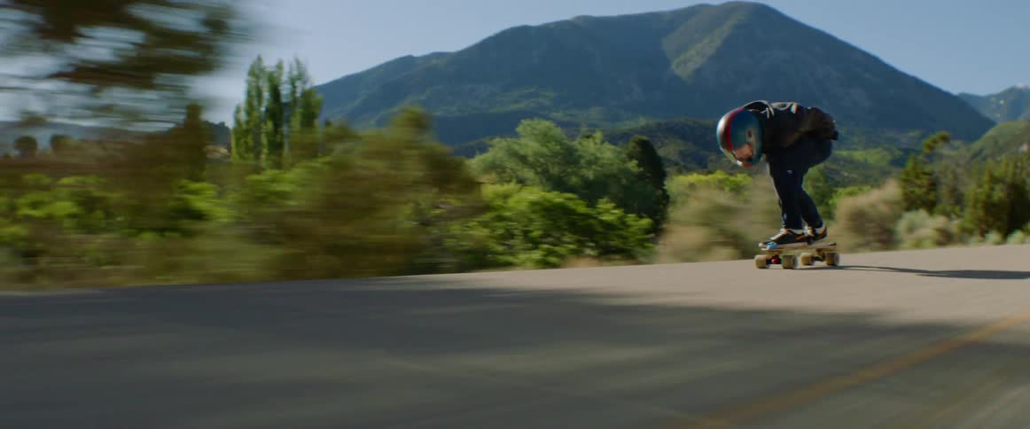 A person leans forward as they skateboard quickly on a rural road
