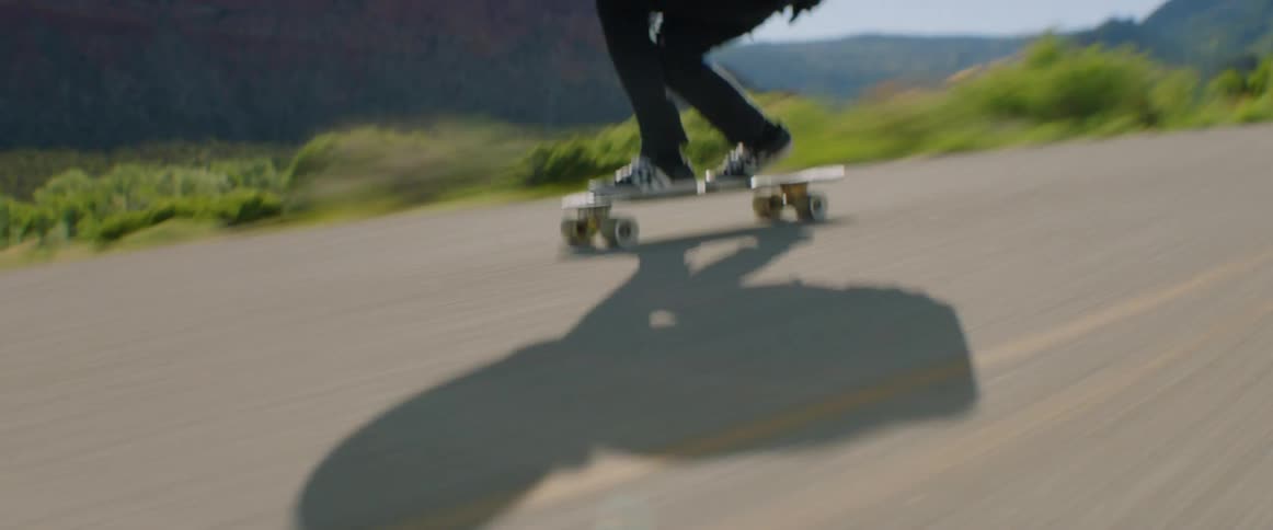 A skateboarder speeding down a paved road with mountains in the distance