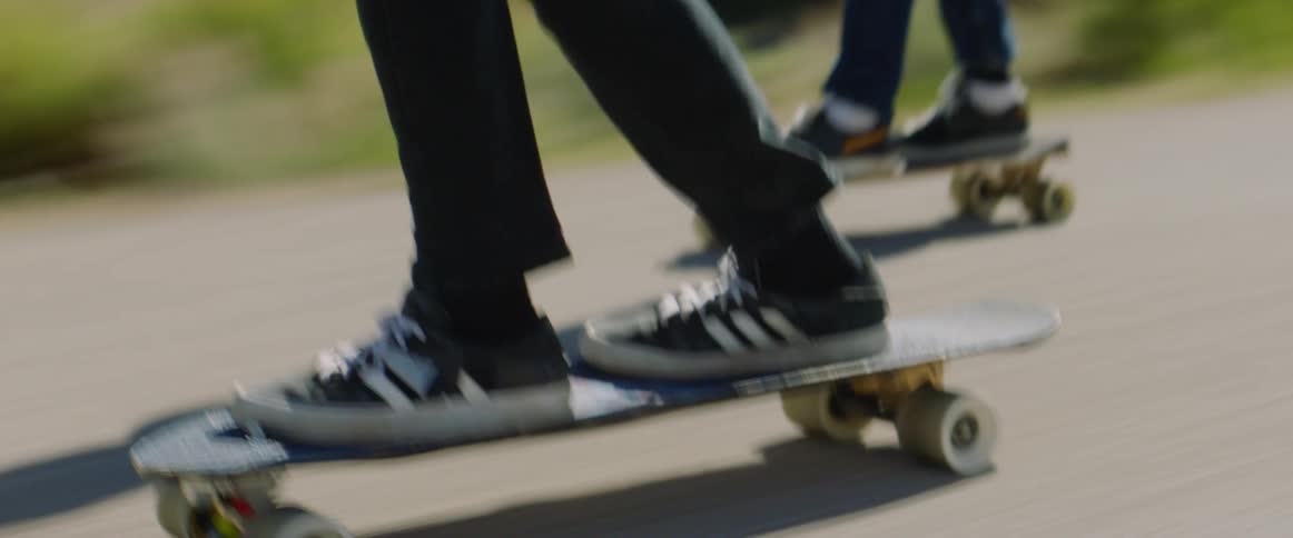 Skateboarders ride skateboards along highway past scrub and mountains