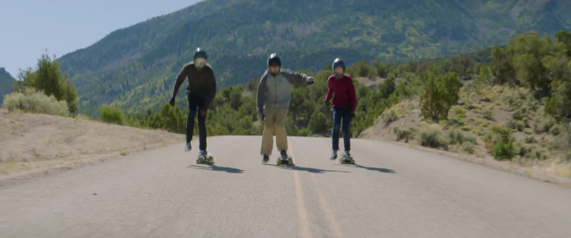 Three teenagers race on skateboards down a street
