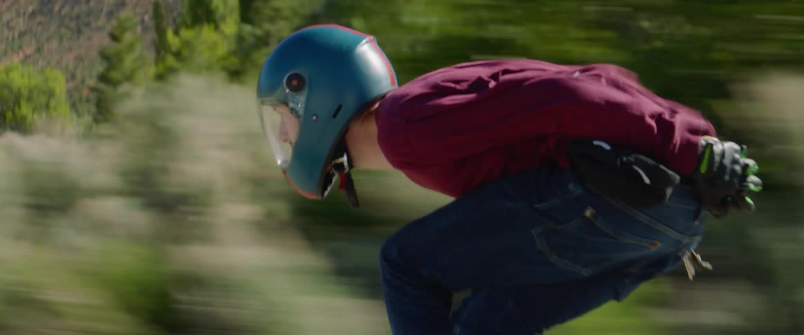 Two skateboarders ride past scrub wearing helmets