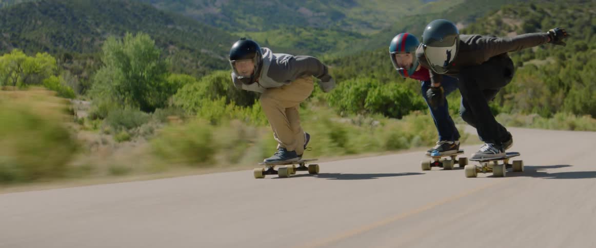 Skateboarders ride downhill on a winding road at high speed