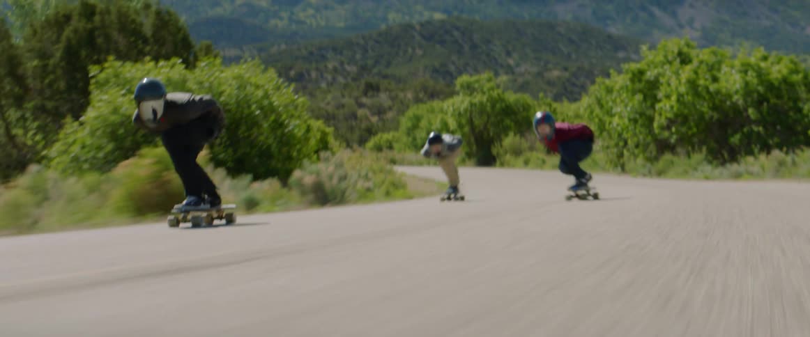 Three people racing down a street on skateboards