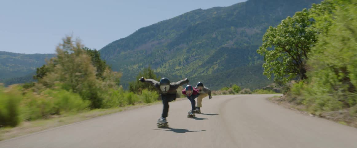 Skateboarders speeding down a paved road in mountains on a summer day