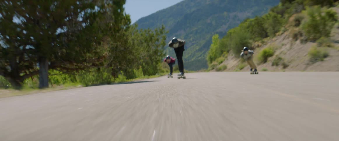 Group of friends wearing crash helmets and protective gloves ride longboards downhill at full speed
